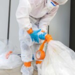 Technician in full protective gear sealing asbestos waste during safe removal process